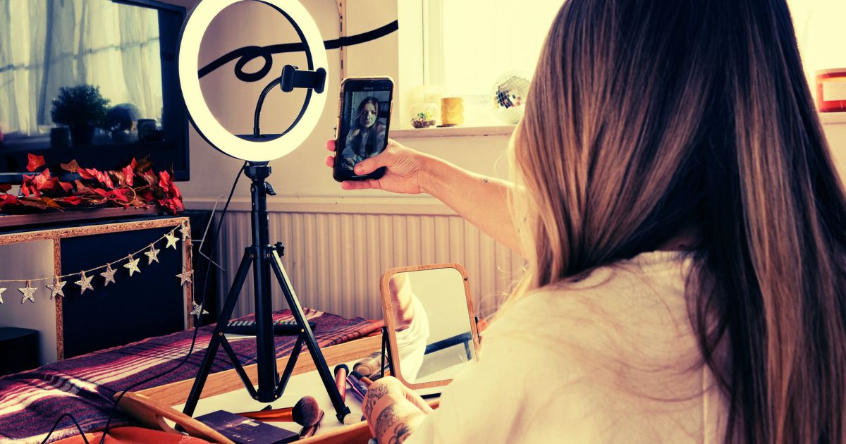 Uma pessoa gravando uma selfie vdeo para fazer um marketing de vdeo. Atrs uma luz branca e espelhos.