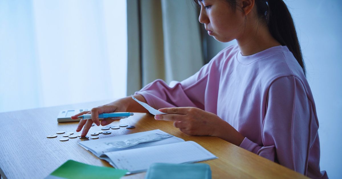 Mulher segurando caneta e papel enquanto faz contas, com calculadora, moedas e fatura sobre a mesa, representando organizao financeira.