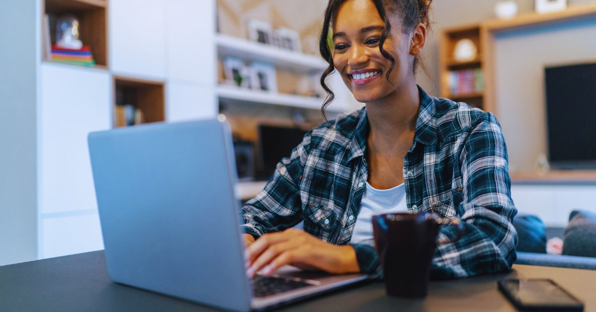 Mulher feliz trabalhando em casa com notebook e uma caneca de caf, representando renda extra em 2025