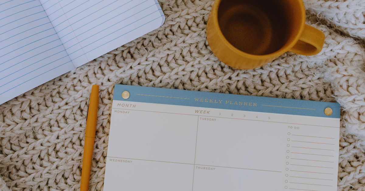 Calendrio com caderno, caneta e caneca de caf sobre a mesa, representando organizao da rotina para renda extra