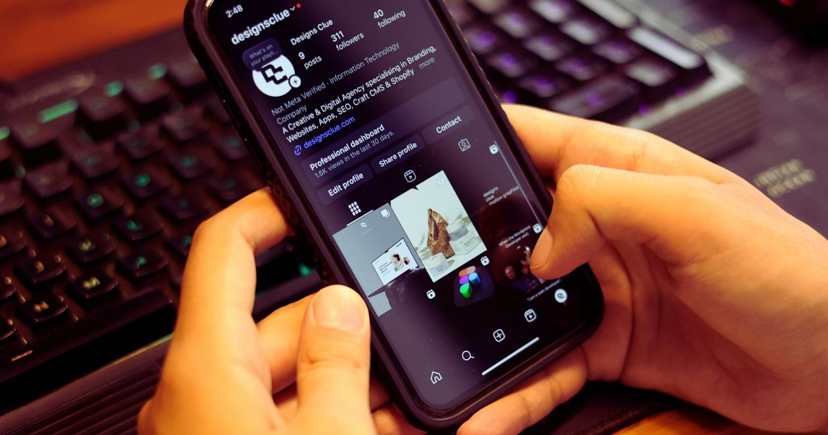 Mãos segurando um celular exibindo uma rede social empresarial, com notebook aberto ao fundo representando gestão de mídias sociais para empresas