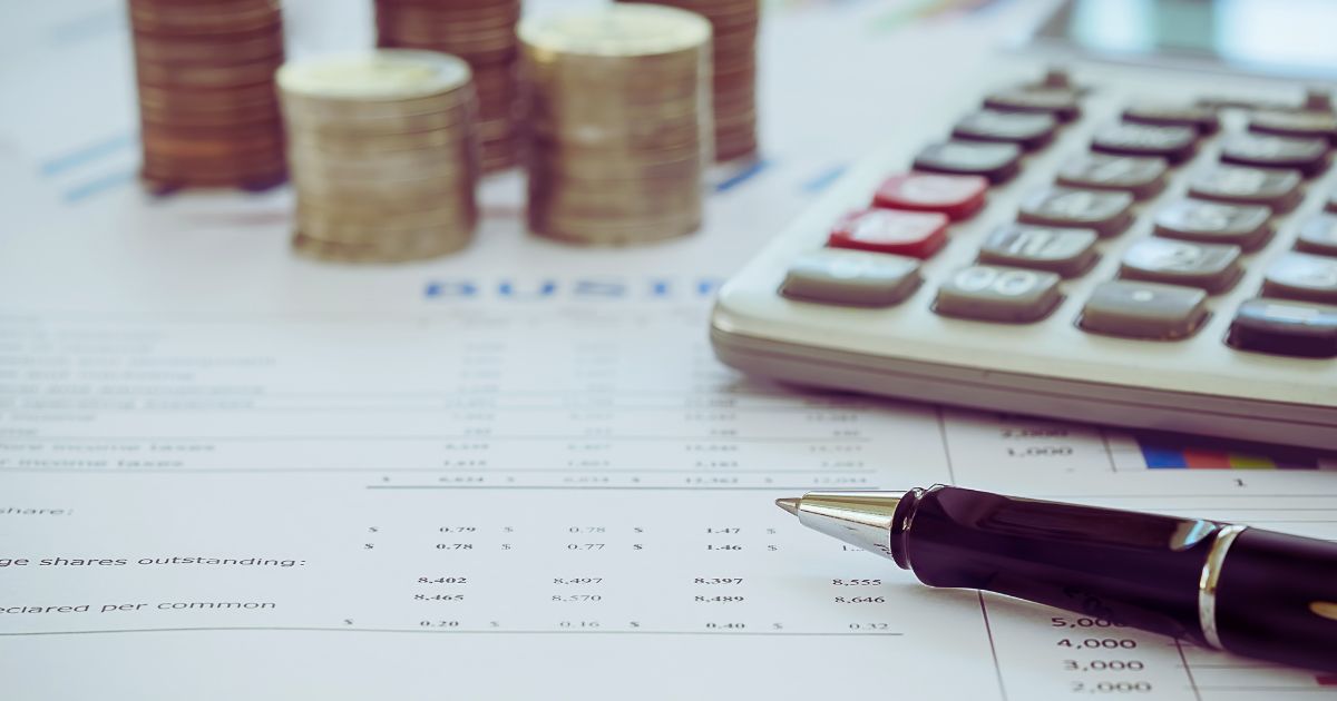 caneta, papeis, tabelas e uma calculadora ao lado de um notebook, representando organização financeira