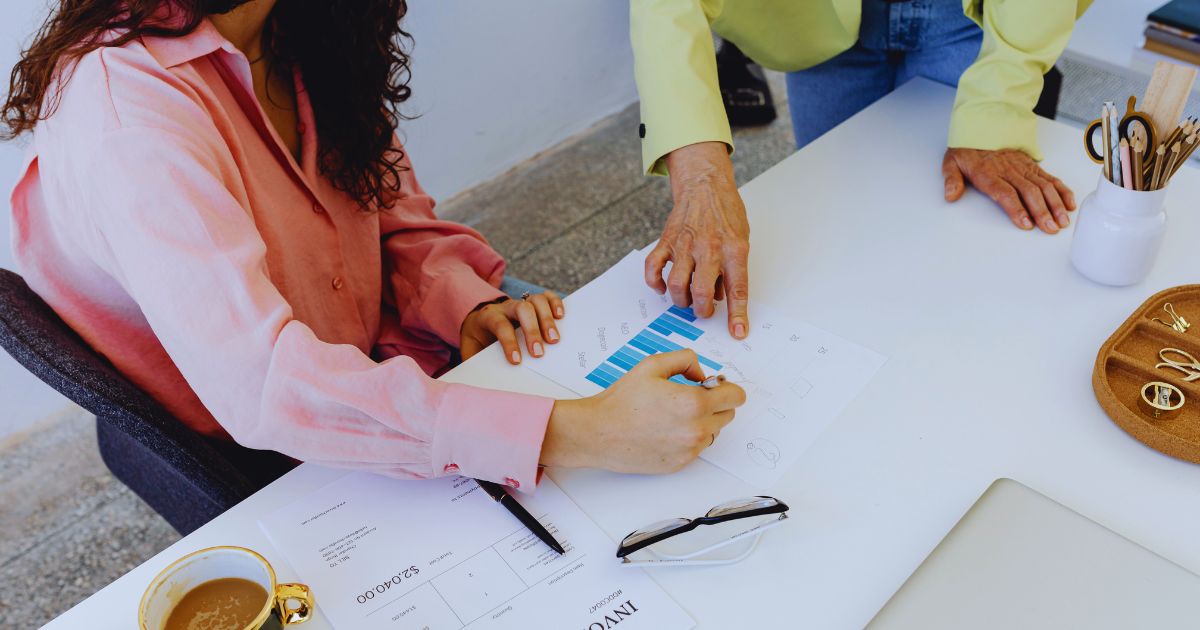Duas pessoas analisando gráficos de crescimento em uma mesa com papéis, café e materiais de escritório, representando estratégias de sucesso em marketing de afiliados.