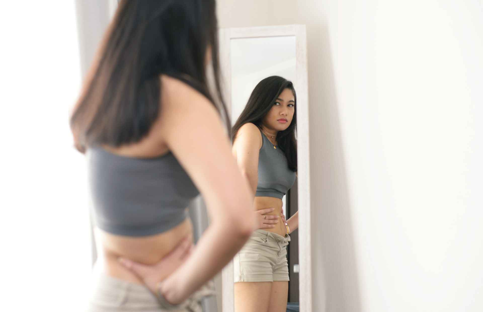 woman staring in the mirror and not liking her body